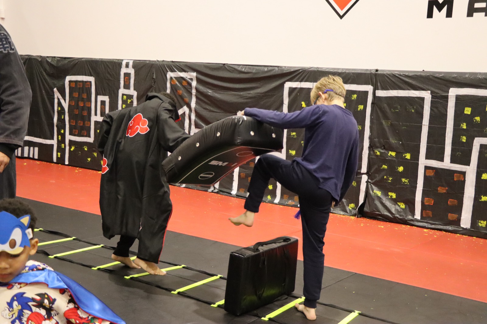 A child in pajamas vaulting over a training pad on an agility ladder during the parkour course.